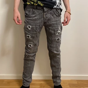 Grå slitna jeans från Alessandro Zavetti - Grå jeans från Alessandro Zavetti med coolt sliten look och flera revor framtill. Modellen har fem fickor, dragkedja och knapp i midjan. Jeansen är i smal passform och tillverkade i mjukt bomullstyg med stretch för extra komfort.