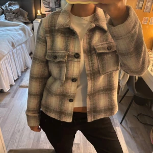 Rutig overshirt från ONLY i pastell - Säljer en supermjuk och trendig rutig overshirt från ONLY i beige, grått och ljusrosa. Jackan har stora bröstfickor med knappar, klassisk krage och knäppning framtill. Perfekt att slänga över en hoodie eller t-shirt för en chill look. Jackan är kanppt använd alls!