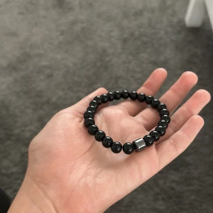 Svart pärlarmband från Rovior - Stilrent svart armband från Rovior med blanka pärlor och en cool silverfärgad detalj. Elastiskt band gör det enkelt att ta på och av. Kommer i en snygg svart påse med Rovior-logga – perfekt att ge bort eller ha själv.