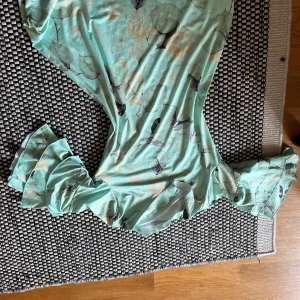 Mintgrön blommig långklänning S - Superfin mintgrön långklänning med blommigt mönster i ljusa och grå toner. Klänningen har volangdetaljer vid ärmarna och en figurnära passform som ger en snygg siluett. Perfekt för dig som gillar romantiska och somriga vibes.