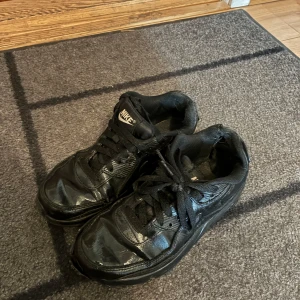 Svarta Nike sneakers i skinn - Säljer ett par helsvarta Nike sneakers i skinn med klassisk design och snörning. Skorna har rund tå och platt sula, perfekt för dig som gillar en clean och sportig look. Passar dig med storlek 37.5. Skorna har hål i sulan.