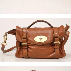 Mulberry brun axelväska i skinn Alexa  - Obs!! Kom inte in här då jag fick problem med min telefon och mejl därav tappade köparen och kunde inte sälja den!! Men nu aktiv igen från just nu! Så återpublicerar då det var länge sedan.  Snygg axelväska från Mulberry i brunt skinn med guldiga metalldetaljer och flätat handtag. Väskan har klassisk Mulberry-logga på framsidan, justerbar axelrem och praktiska spännen. Insidan är fodrad med Mulberry-mönster. Perfekt för dig som gillar stilrena accessoarer. Inga fläckar på insidan mycket fin