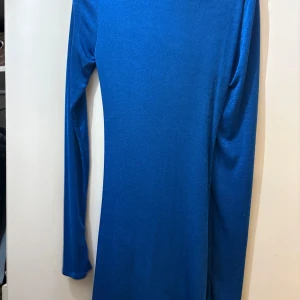 Blå omlottklänning från NLY ONE - Snygg blå kortklänning från NLY ONE med lång ärm och djup v-ringning. Klänningen har omlottdetalj och snygg snörning framtill som ger en cool rynkad effekt. Materialet är mjukt och stretchigt, perfekt för att sticka ut med färg och form.