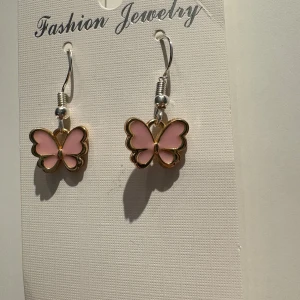 Rosa fjärilsörhängen med guldkant - Superfina örhängen med hängande fjärilar i ljusrosa och guldfärgad kant. Söt design som verkligen poppar och ger en gullig touch till din look. Perfekt för dig som älskar detaljer och vill sticka ut med något unikt.