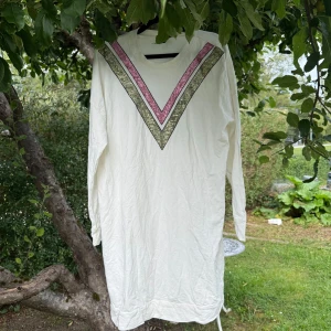 Vit långärmad tröja - Säljer en vit långärmad tröja i storlek XL. Tröjan har ett coolt V-format mönster framtill i rosa och olivgrönt, vilket ger en unik touch. Materialet känns mjukt och skönt, perfekt för dig som gillar enkel men snygg stil. Mer använd men fortfarande fint skick. 