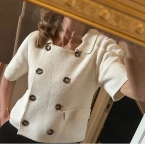 Vit stickad kortärmad kofta med krage Gina Tricot , Stl m - Säljer en Cremevit croppad kofta med korta ärmar och krage. Toppen har dubbelknäppning med stora, mörka knappar framtill.  Materialet är stickat och ger en cool, strukturerad känsla. Slutsåld i butik , nypris 499;-