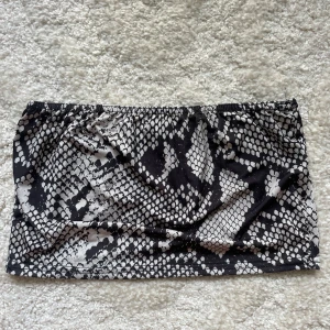 Svartvit snake bandeau  - Säljer en svartvit bandeau tubtopp från Boohoo med coolt ormskinnsmönster. Toppen är axelbandslös och har en elastisk kant upptill för att sitta på plats. Perfekt att styla med höga jeans eller kjol för en edgy look.
