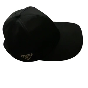 Svart keps från Prada i nylon - Snygg svart keps från Prada med klassisk böjd skärm och justerbart spänne bak. Kepsen har Pradas ikoniska metallogo på sidan och är tillverkad i glansig nylon som ger en lyxig känsla. Perfekt accessoar för en clean och stilren look.