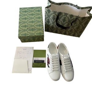 Gucci ace sneakers med orm  - Snygga vita sneakers från Gucci ace  skinn med broderad röd och svart orm på sidan. Skorna har klassisk rund tå, vita snören och grön detalj på hälen. Kommer med originalkartong och tillbehör. Perfekta för dig som vill sticka ut med lyxig streetstyle pris kan diskuteras 