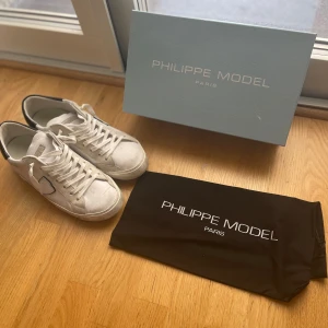 Vita Philippe Model sneakers - Snygga vita sneakers från Philippe Model Paris med svarta detaljer på hälen och klassisk snörning. Dom är använda max 3 gånger så helt i nyskick. Dom är äkta och dom är köpta från merchsweden. Box påse och tag medföljer.