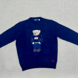 Blå stickad tröja Polo Bear Ralph Lauren - Säljer en blå stickad tröja från Polo Ralph Lauren med ikonisk Polo Bear-motiv på bröstet och RL-broderi i rött vid nederkanten. Tröjan har rund hals och långa ärmar, perfekt för dig som gillar klassisk streetstyle med en twist.