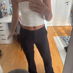 Marinblåa kostymbyxor  - Säljer ett par marinblåa kostymbyxor  med hög midja och dragkedja framtill. Byxorna har en snygg söm längs benen och sitter tajt upptill men släpper ut vid anklarna. Perfekta om du gillar en stilren och trendig look.