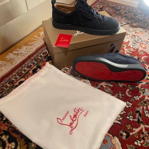 Mörkblå sneakers från Christian Louboutin - Snygga mörkblå sneakers från Christian Louboutin i mocka med klassisk röd sula och diskret broderad logga på hälen. Skorna har rund tå, svarta snören och en stilren design som sticker ut med den ikoniska röda undersidan. Det är mycket bra skick men den har bara en liten liten brun fläck längst fram som man kan ta bort med papper. Vill av med dem för ville egentligen köpa andra skor! Ni kan alltid diskutera med mig över minsta fråga såsom pris och detaljer mm. Välkommen!😊✌️(Bor i Uppsala)