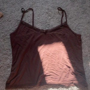 Brun linnetopp med spets från Nelly - Snygg brun linnetopp från Nelly i storlek XL. Tunn bomullskänsla med smala axelband och spetsdetaljer längs halsringning och nederkant. 