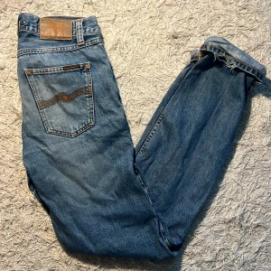 Nudie Jeans Gritty Jackson Far Out 28/32 - Säljer ett par blå Nudie Jeans Gritty Jackson Far Out i 100% bomull. Klassisk femficksmodell med orange sömmar och Nudie-logga på bakfickan. Raka ben och normal passform. Säljes då de inte passar längre. Enda slitaget man skulle kunna märka på är att de längst ner är något slitna.