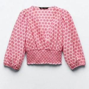 Rosa blommig blus från Zara - Supersöt blus från Zara i ljusrosa med blommigt mönster i mörkare rosa. Blusen har långärmade puffärmar, v-ringad hals och smockad midja som ger en snygg siluett.