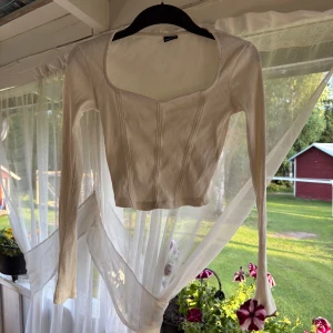Vit ribbad korsettopp Gina Tricot  - Supersnygg vit ribbad korsettopp från Gina Tricot i storlek XS. Toppen är croppad med långa ärmar, markerade sömmar framtill och en snygg sweetheart-urringning. Perfekt att styla med jeans eller kjol för en trendig look.