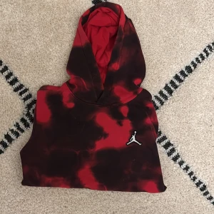 Jordan hoodie röd och svart M - Säljer en Jordan hoodie i storlek M med röd och svart batikmönster. Tröjan har huva, broderad Jumpman-logga på bröstet och Michael Jordans signatur på ärmen. Mjuk insida i bomullsmix, perfekt för chill och streetwear.
