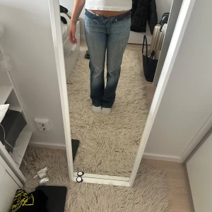 Lågmidjade bootcut jeans blå - Säljer ett par blå lågmidjade jeans med bootcut-snitt. Jeansen har klassisk femficksdesign, ljus tvätt och subtila slitningar. Snygg passform som sitter tajt upptill och släpper vid benen. Perfekta för dig som gillar retrovibbar och vill ha en avslappnad men trendig look.