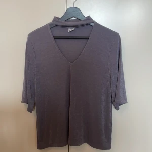 Lila v-ringad topp från Gina Tricot - Säljer en lila topp från Gina Tricot med v-ringning och liten ståkrage. Modellen har trekvartsärm och är gjord i ett mjukt, lätt glansigt material som känns skönt mot huden. Passar bra till mer festliga tillfällen!
