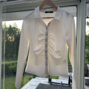 Vit långärmad skjorta från Bik Bok - Snygg vit skjorta från Bik Bok med lång ärm och klassisk krage. Skjortan har knappar framtill och rynkdetalj längs knappraden. Skjortan har lite strech och är mjuk att ha på. Endast använd en gång för att testa. Passar även en person som har M i storlek. 