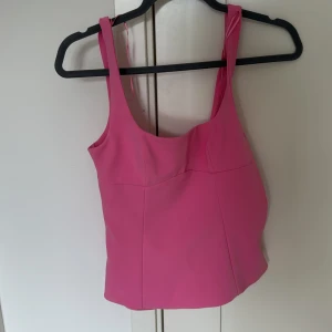 Rosa topp med rosett från Zara - Superfin rosa topp från Zara med breda axelband och en stor rosett i ryggen. Toppen har en snygg, figurnära passform och är tillverkad i ett mjukt polyestermaterial. Dragkedja i sidan för enkel påklädning. Lappen är kvar och toppen är bara testad💕