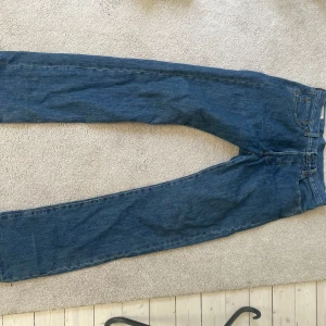 Levi's 501 blå jeans W31 L34 - Klassiska Levi's 501 jeans i blå denim med raka ben och normal passform. Byxorna har fem fickor, knappgylf och den ikoniska läderpatchen bak i midjan. Perfekta för dig som gillar tidlös stil och vill ha ett par schyssta jeans i bomull.