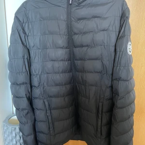 Svart pufferjacka från Vinson Polo Club - Svart pufferjacka från Vinson Polo Club med huva och dragkedja framtill. Jackan har ett stilrent badge på ärmen och är quiltad med horisontella sömmar. Perfekt för kyliga dagar och enkel att matcha med det mesta. Skriv vid fler frågor eller bilder! 💕