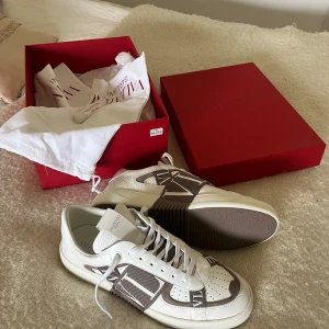 Valentino VL7N 2.0 sneakers i vitt och beige - Säljer mina Valentino VL7N 2.0 sneakers i vitt skinn med beige detaljer nu till sommarn då jag har ett annat par redan och därav ingen användning till dem. Kommer med originalkartong och dustbag. Köpta för 7800 kr på Selfridges i London. Ungefär de priset den färgen ligger på nätet för också. Använda 4-5 gånger. Hör gärna av er om ni har frågor! Mvh Hampus 