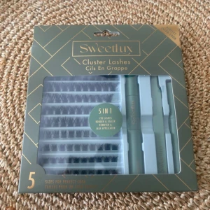 Sweetlux Cluster Lashes 5-i-1 kit - Sweetlux Cluster Lashes 5-i-1 kit med lösögonfransar i olika storlekar, lim, sealer, remover och applikator. Perfekt för att skapa fylliga fransar hemma. Förpackningen är grön med guldiga detaljer.