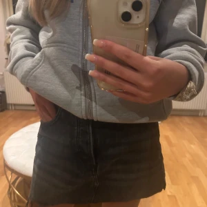Svart jeanskjol med hög midja - Säljer en svart jeanskjol med hög midja och klassiska fickor fram. Kjolen har en kort passform och stängs med knapp och dragkedja. Perfekt för dig som gillar en enkel och stilren look.