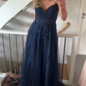 Marinblå balklänning - Säljer min balklänning, endast använd en gång och har inga defekter, mycket spets och har fina blommdetaljer, den har även en slits på vänster sida. Perfekt för bal eller festliga tillfällen.💕💕