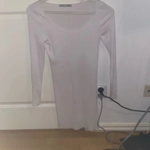 Vit ribbad långärmad klänning - Säljer en vit, tight ribbad klänning med lång ärm och rundad urringning. Klänningen är kort och har en enkel, stilren design som passar perfekt till många tillfällen. Materialet är stretchigt och bekvämt.