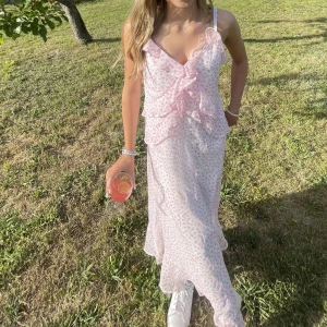 Ljusrosa blommig långklänning med volang - Säljer denna söta ljusrosa långklänning med små blommor och volangdetaljer framtill. Klänningen är ärmlös med smala axelband och är perfekt för sommarens tillfällen.🌸