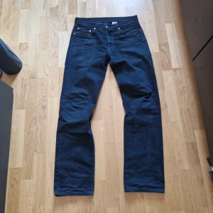 Levi's 501 svarta jeans - Klassiska svarta Levi's 501 jeans i 100% bomull. Rak passform med knappgylf och fem fickor. Perfekta för dig som gillar tidlös stil och vill ha ett par jeans som funkar till det mesta.