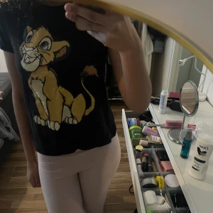 Svart t-shirt med Simba-tryck - Svart t-shirt med stort tryck av Simba från Lejonkungen på framsidan. Klassisk rund hals och korta ärmar. Perfekt för dig som älskar Disney och vill ha en lekfull stil.