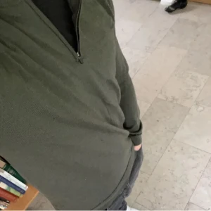 Mörkgrön Merinoulltröja med dragkedja i kragen - Säljer en mörkgrön half zip tröja med krage och dragkedja framtill. Tröjan har ribbade muddar vid ärmslut och nederkant. Perfekt för lager-på-lager och enkel att matcha med olika outfits. OBS tröjan är inte ifrån polo Ralph Lauren, märket heter Shaping New Tomorrow