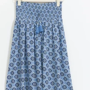 Blå mönstrad långkjol med tofsar - Säljer en blå långkjol med vitt och mörkblått grafiskt mönster. Kjolen har smock i midjan och dekorativa tofsar framtill. Perfekt för dig som gillar bohemisk stil och vill ha något luftigt och snyggt.