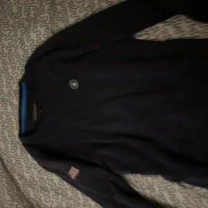 sail racing tröja - Mörkblå långärmad tröja från Sail Racing med broderad USA-flagga på ärmen och stort 'USA 77' tryck på ryggen. Blå insida vid kragen och rund hals. Perfekt för dig som gillar sportig stil.