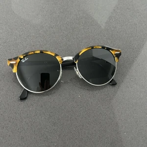 Runda solglasögon från Ray-Ban med sköldpaddsmönster - Snygga runda solglasögon från Ray-Ban med sköldpaddsmönstrad ram i brunt och svart. Glasen är mörka och bågarna har metall- och plastdetaljer. Perfekt accessoar för att lyfta din stil.
