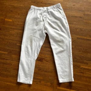 Vita linnebyxor - Säljer ett par vita linnebyxor med avslappnad passform och resår i midjan. Byxorna har raka ben och sidofickor framtill samt fickor bak. Perfekta för varma dagar och enkel stil.