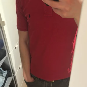 Röd pikétröja från Ralph Lauren - Säljer en klassisk röd pikétröja från Ralph Lauren med liten broderad logga på bröstet. Tröjan har korta ärmar och krage med knappar. Perfekt för en stilren och avslappnad look. M men känns som S
