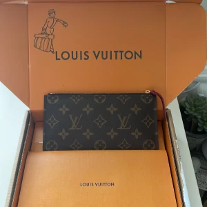 Monogram plånbok från Louis Vuitton - Säljer en klassisk plånbok från Louis Vuitton med ikoniskt monogrammönster i brunt och beige. Väskan har dragkedja upptill och insida i mörkrosa. Perfekt accessoar för att lyfta din outfit.