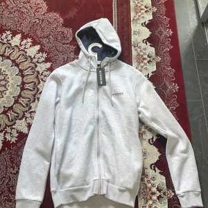 Ljusgrå hoodie från McKenzie - Säljer en stilren ljusgrå hoodie från McKenzie i storlek M. Tröjan har dragkedja framtill, huva med snörning och ribbade muddar vid ärmslut och nederkant. Perfekt för en avslappnad look. Inte använd en gång efter som den är för stor för mig. 
