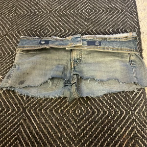 Ljusblå jeansshorts med fransar - Säljer ett par ljusblå jeansshorts med råa, fransiga kanter och dubbla knappar i midjan. Det är stearin på shortsen som inte går bort så säljer dom bara för 10kr. Klassisk femficksmodell med slitna detaljer och låg midja. Perfekta för varma dagar och en avslappnad stil.