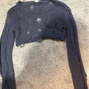 Mörkgrå croppad stickad tröja från Zara - Säljer en mörkgrå croppad stickad tröja från Zara med trasiga detaljer och lång ärm. Perfekt för dig som gillar en edgy och trendig stil. Tröjan har en lös passform och är superenkel att styla till olika outfits.