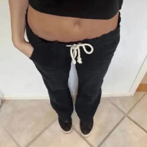 Mörkblå linnebyxor från Roxy - Mörkblå linnebyxor från Roxy med vit snörning i midjan och raka ben. Byxorna har resår i midjan och två bakfickor. Perfekta för en avslappnad stil och sköna att bära under varmare dagar.