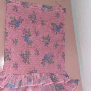 Rosa blommig klänning med volang - rosa kjol med blommigt mönster och smockad överdel. Nederdelen har en volangkant.