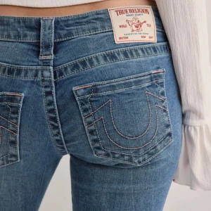  True Religion Jeans - Säljer ett par klassiska blå jeans från True Religion med bootcut och snygga detaljerade bakfickor. Jeansen har låg midja och är i ett mjukt denimtyg med lätt tvättad look. Perfekta för dig som gillar en tidlös jeansstil. Dem är fett snygga men jag passar inte i sånnahär typ av blå jeans drf säljer jag💕💕