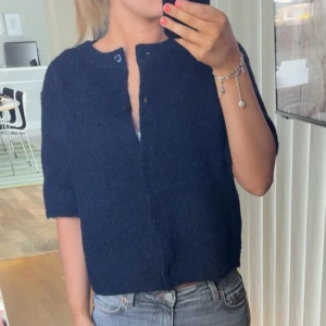 Stickad T-shirt med knappar - Säljer en mörkblå stickad kofta med korta ärmar och knappar framtill. Koftan är från ginatricot (Young) i storlek 158/164